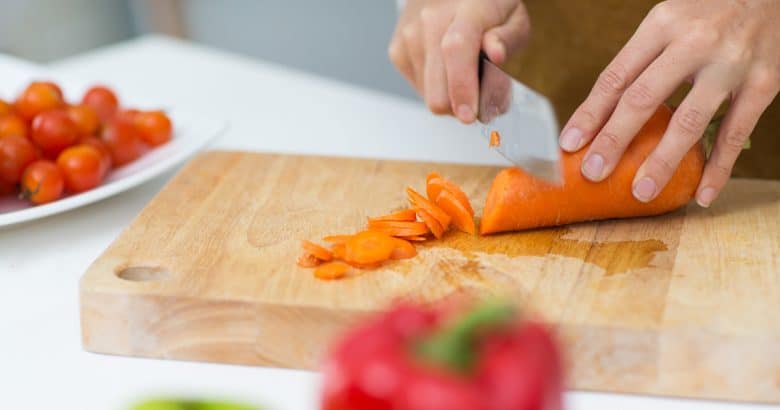dieta vegana - close up de maos cortando cenoura na tabua de cortar