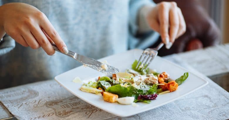 erros da dieta vegana | Mãos de mulher com salada Caesar na mesa no restaurante